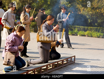 Chine Pékin jeunes Chinois bouddhistes brûlent de l'encens et s'agenouiller pour prier à l'extérieur du palais de la paix et l'harmonie Yonghegong Lama le tem Banque D'Images