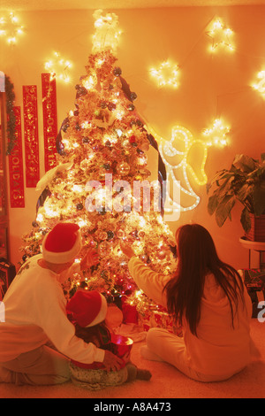 Famille de trois générations assis sous l'arbre de Noël lumineux Banque D'Images