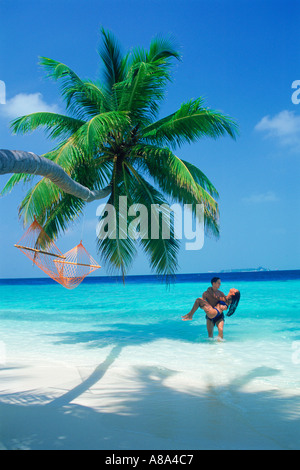 Homme portant femme de couleur aqua eaux sous palm tree Banque D'Images