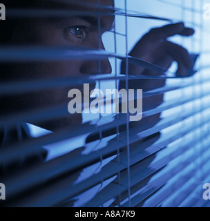 Man looking through blinds Banque D'Images