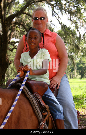 Femme de race blanche et de l'afro-américain jeune fille l'équitation dans le parc. Banque D'Images