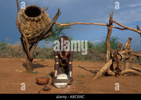 Hamer girl broyer le maïs à côté d'un grenier , Turmi, Sud Vallée de l'Omo, en Ethiopie Banque D'Images