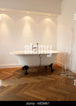 Salle de bains design avec éclairage halogène parquet chevrons et baignoire sur pieds Banque D'Images