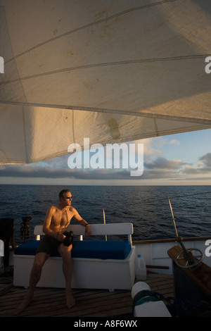 Homme assis sur le pont d'un bateau à voile Banque D'Images