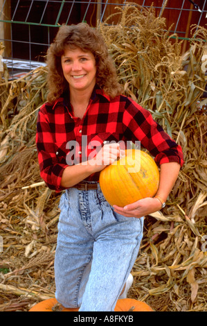 Belle femme de 30 ans en chemise à carreaux holding pumpkin en face de tiges de maïs. Buffalo Minnesota USA Banque D'Images