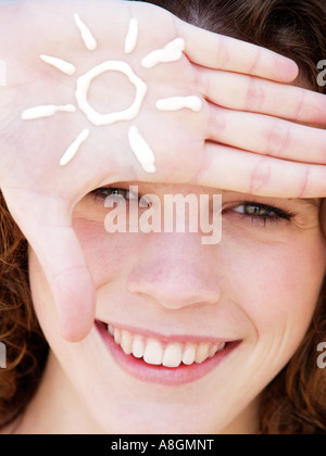 Teenage girl smiling avec la figure d'un soleil dessiné dans la crème solaire sur sa main la peau juste besoin d'être protégé contre le rayonnement UV Banque D'Images