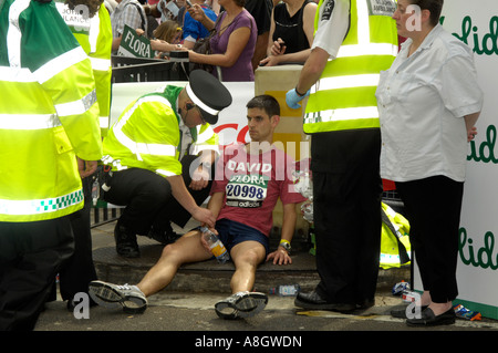 Épuisé runner au Flora London Marathon étant pris en charge par les médecins de deux kilomètres de la ligne d'arrivée Banque D'Images