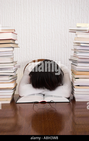 Jeune femme dormir à la tête de la table, les bras croisés sur le livre ouvert Banque D'Images