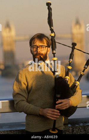 Busker jouant à la cornemuse pour collecter de l'argent auprès des employés de bureau sur London Bridge. Tower Bridge est en arrière-plan. LONDRES 1990S 1992 ROYAUME-UNI HOMER SYKES Banque D'Images