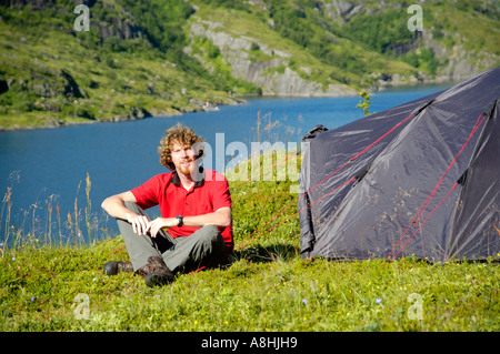 Monsieur le jeune homme s'assied à sa tente dans le désert de Moskenesoya avec Agvatnet Norvège Lofoten Banque D'Images