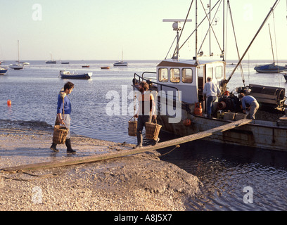 les archives des années 1980 voient des hommes sur une planche de marche à l'aide de chapes d'épaule Pour transporter des paniers de poisson de coquillages du bateau de pêche 80s Leigh Sur Sea Southend Essex Angleterre Royaume-Uni Banque D'Images