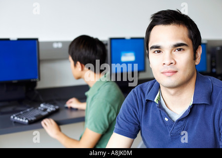 Portrait d'un jeune homme souriant avec un jeune homme assis derrière lui et à l'aide d'un ordinateur Banque D'Images