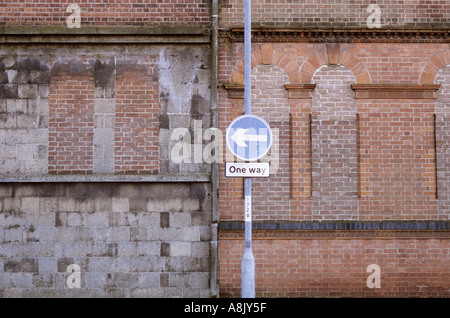 Signer avec la flèche indiquant un sens fixé sur un lampadaire en face de vieux bâtiments en brique avec windows murée Banque D'Images