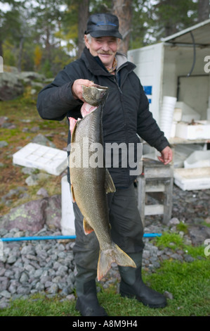 Un Sami fisherman holding up l'une des prises du matin, pris dans un lac local ; Stora Sjöfallet Parc National, Laponie, Suède. Banque D'Images