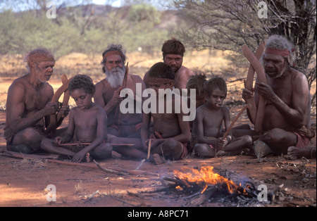 Les aînés autochtones et les garçons peint pour chanter avec rituel cérémonie clapsticks en regard de feu dans le désert de l'Australie centrale à distance Banque D'Images