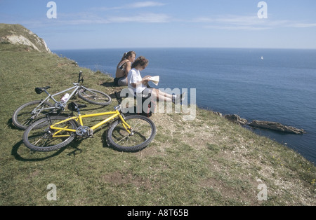 Deux filles 2 vélos à côté de repos sur des falaises au-dessus de Lulworth Ouest Banque D'Images
