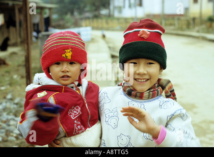 Souriante jeune fille exerçant son cadet, portant des chapeaux et foulards laineux, Bac Ha, province de Lao Cai, NW Viet Nam Banque D'Images