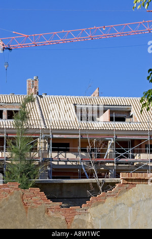 Nouveau bâtiment ou site de construction avec grue vu à travers un vieux mur cassé lors d'une journée ensoleillée avec un ciel bleu Banque D'Images