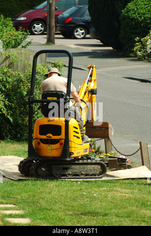 Homme conduisant une minipelle hydraulique de pose de chenille rampant à travers la pelouse de jardin avant domestique sur des feuilles de protection contre le contreplaqué Essex Angleterre Royaume-Uni Banque D'Images