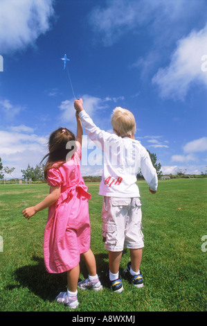 Boy and girl flying kite together in park Banque D'Images