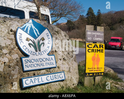 Le Parc National de Snowdonia bilingue signe sur un rocher à côté de la criminalité voiture panneau d'avertissement dans le parking. Capel Curig North Wales UK Banque D'Images