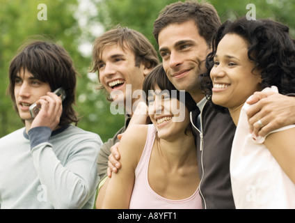 Groupe de jeunes amis, l'un souriant using cell phone Banque D'Images