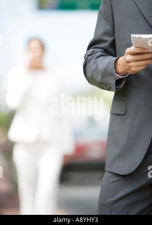 Man holding portable, vue partielle, silhouette de femme en costume dans l'arrière-plan Banque D'Images