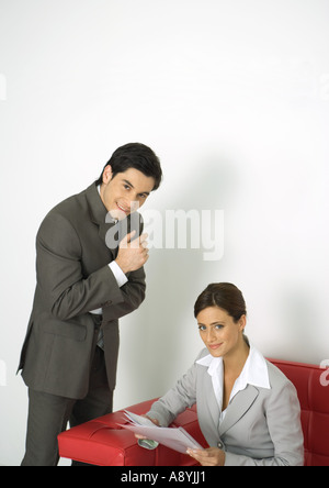 Businessman standing next to businesswoman assis sur le canapé, les deux smiling Banque D'Images