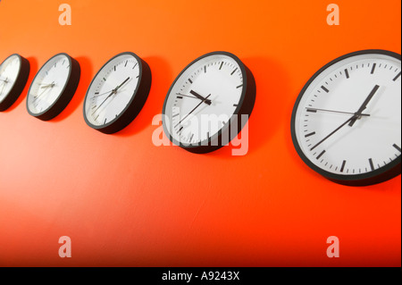 Rangée d'horloges sur un mur orange Banque D'Images