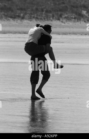 Young man carrying woman piggy back pour garder ses pieds au sec, Enniscrone / Inishcrone, Comté de Sligo, Irlande Banque D'Images