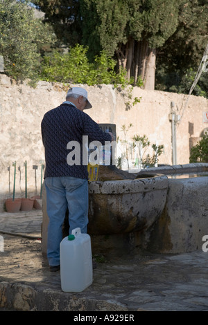 L'homme d'eau de remplissage des bouteilles sur l'approvisionnement en eau de la fontaine Scopello Sicile Italie Banque D'Images