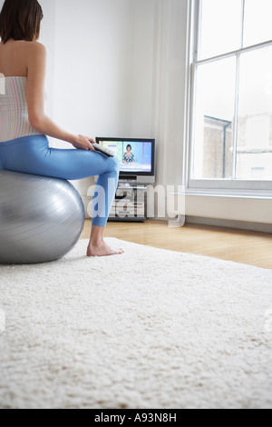 Woman sitting on fitness ball, regarder la télévision, vue arrière Banque D'Images