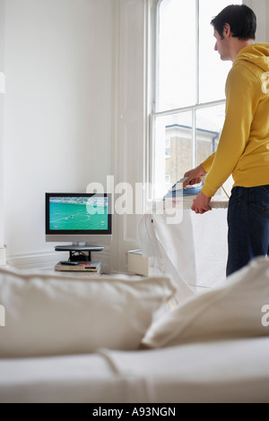 L'homme le repassage et regarder la télévision Banque D'Images