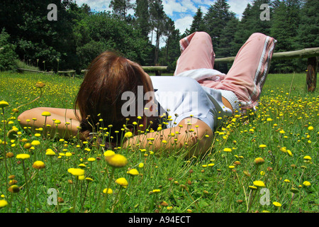 Une jeune femme allongée sur le dos la rêverie dans une verte prairie parsemée de fleurs jaunes de l'Afrique du sud du cap de l'Est Banque D'Images