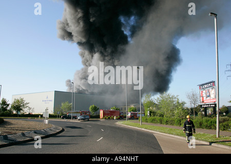 Le pompier s'éloigne de l'immense panache de fumée sur le feu à l'entrepôt médical coleraine Banque D'Images