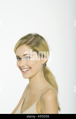 Teenage girl with cuillerée de fondation sur joue, smiling at camera Banque D'Images