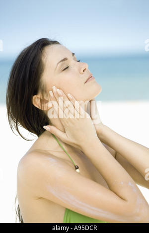 Femme avec un écran solaire sur le bras, les mains de chaque côté du visage, les yeux fermés Banque D'Images