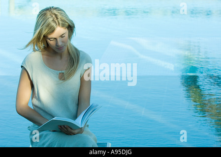 Jeune femme assise par l'eau, lecture Banque D'Images