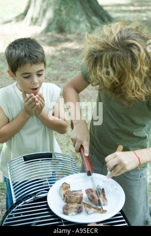 Garçon découpage morceau de viande grillée tout en deuxième garçon montres Banque D'Images