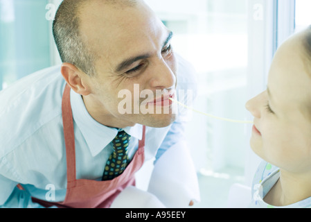 Père et fille holding extrémités de noodle en bouche, smiling Banque D'Images