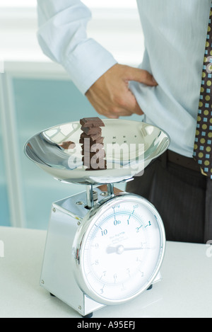 Pile de morceaux de chocolat sur l'échelle, et l'homme cuisine taille pincement Banque D'Images