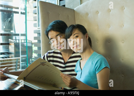 Young couple sitting in restaurant, menu holding Banque D'Images