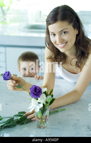 Jeune femme faisant arrangement de fleurs fraîches, next to boy, smiling Banque D'Images