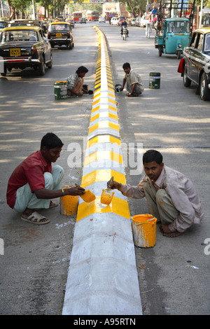 Jeunes garçons indiens peignant des marquages routiers avec de la peinture jaune et noire sur le séparateur de voies, Mumbai, Inde Banque D'Images