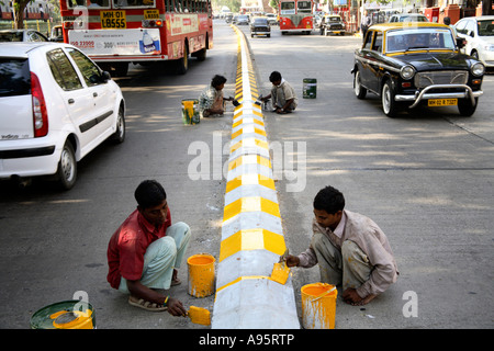 Jeunes garçons indiens peignant des marquages routiers avec de la peinture jaune et noire sur le séparateur de voies, Mumbai, Inde Banque D'Images