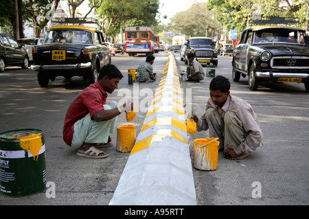 Jeunes garçons indiens peignant des marquages routiers avec de la peinture jaune et noire sur le séparateur de voies, Mumbai, Inde Banque D'Images