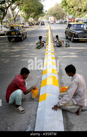 Jeunes garçons indiens peignant des marquages routiers avec de la peinture jaune et noire sur le séparateur de voies, Mumbai, Inde Banque D'Images