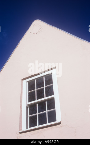 Détail de fenêtre à guillotine peint en blanc avec des petits volets carrés récemment en rose recouvert de pignon de maison sous ciel bleu profond Banque D'Images