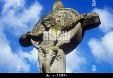 Détail de ciment recouvert de lichen sur Jésus Christ en croix celtique avec ciel bleu et nuages cumulus derrière Banque D'Images