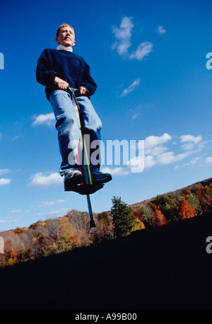 À la recherche jusqu'à un adolescent de rebondir sur un Pogo Stick avec feuillage d'automne dans l'arrière-plan Banque D'Images